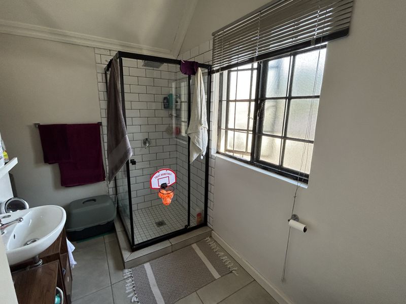 A functional bathroom featuring a glass-enclosed shower with subway tiling, a pedestal basin, and a window providing natural light.