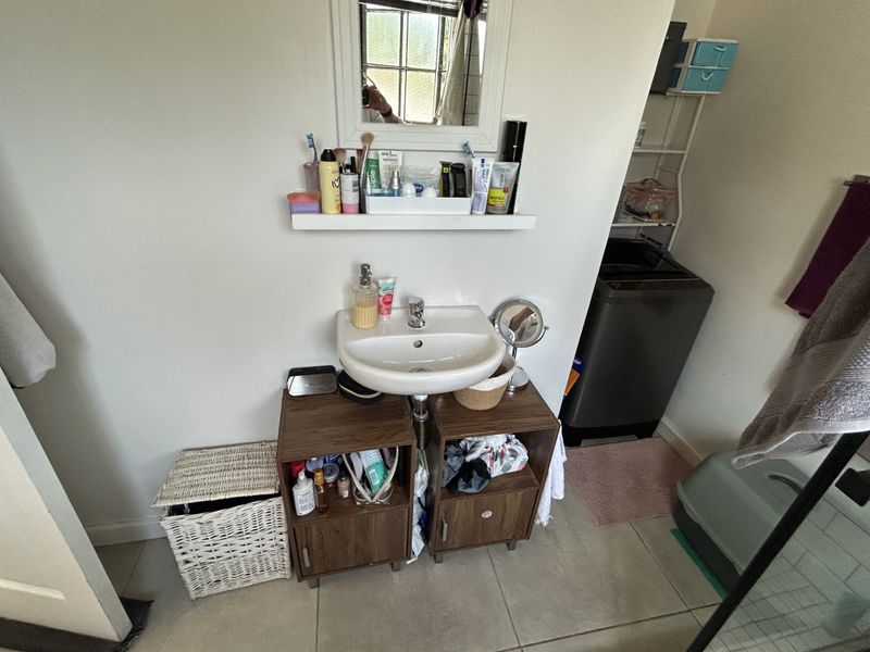 A functional bathroom area featuring a pedestal washbasin with a chrome mixer tap, wall-mounted mirror, and tiled flooring.