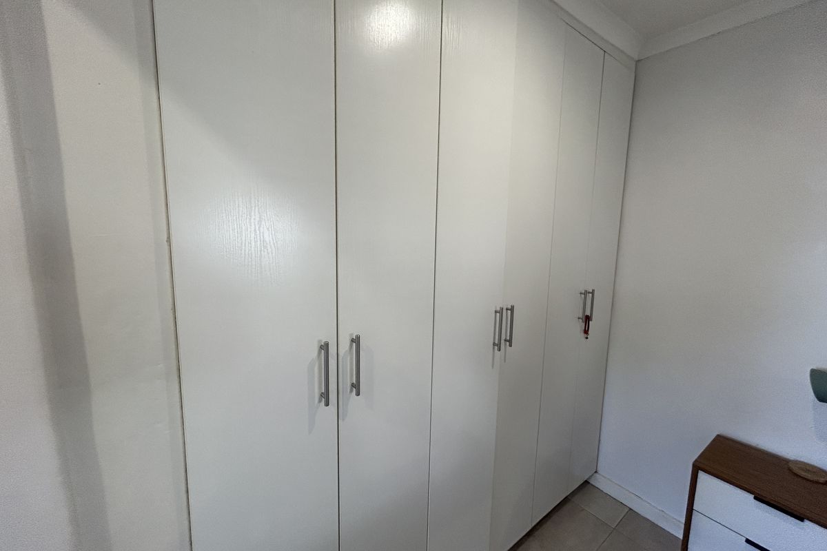 A bedroom featuring white built-in cupboards with modern metal handles, providing ample storage space.
