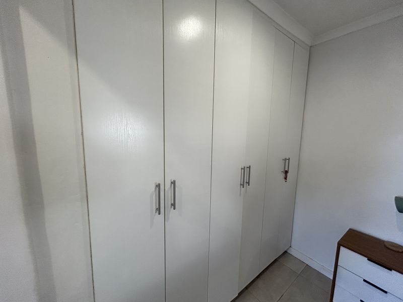 A bedroom featuring white built-in cupboards with modern metal handles, providing ample storage space.