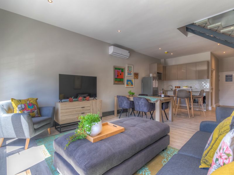 A modern open-plan living and kitchen area featuring neutral tones, contemporary cabinetry, recessed lighting, and a staircase leading to the upper level.