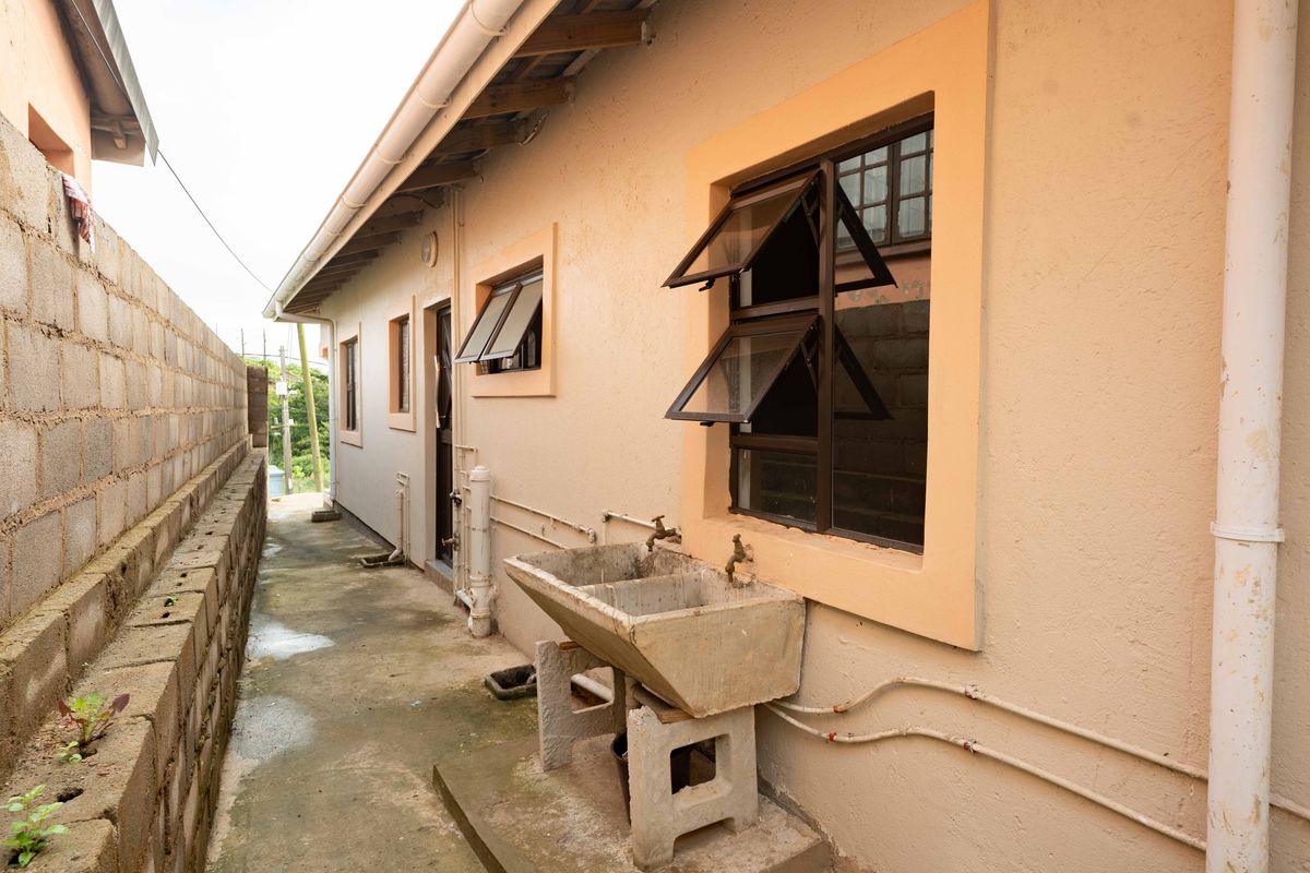 Side exterior view of the property featuring a concrete laundry basin, exposed plumbing, and a concrete pathway alongside a boundary wall.