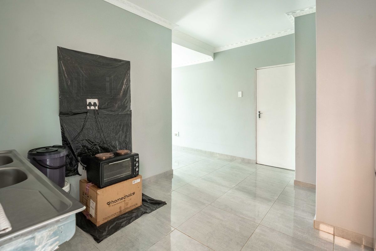 A functional kitchen area featuring tiled flooring, crown molding, and a stainless steel sink unit, leading into an adjacent living space.
