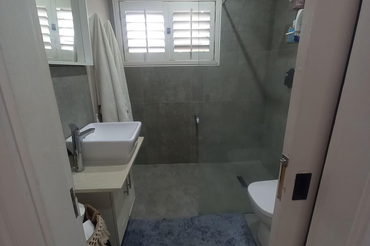 Modern bathroom featuring a walk-in shower with a rain shower head, a sleek countertop basin, and plantation shutters for privacy.