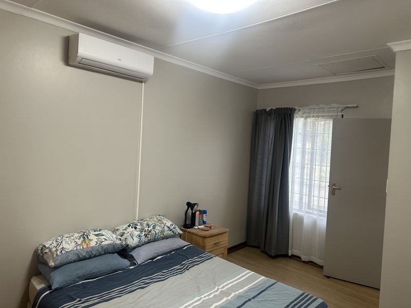 A well-maintained bedroom featuring laminate flooring, a wall-mounted split-system air conditioner, and window security bars for added peace of mind.