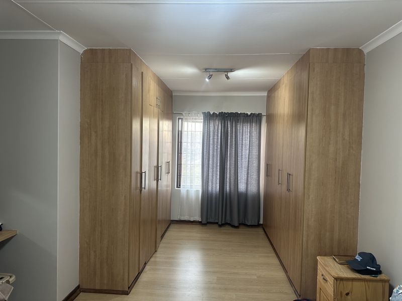 A bedroom featuring extensive floor-to-ceiling built-in wooden cupboards, laminate flooring, and a window with security bars.
