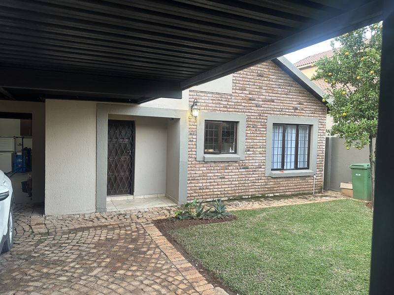 Front exterior view of a townhouse featuring a brick facade, covered carport, paved driveway, and a small private garden area.