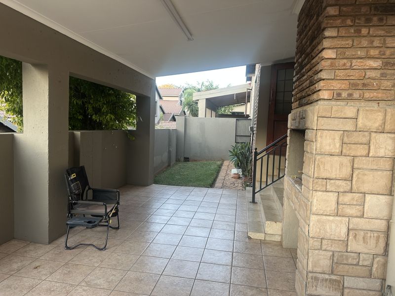 Covered patio area featuring tiled flooring and a built-in brick fireplace, leading to a small private garden space.