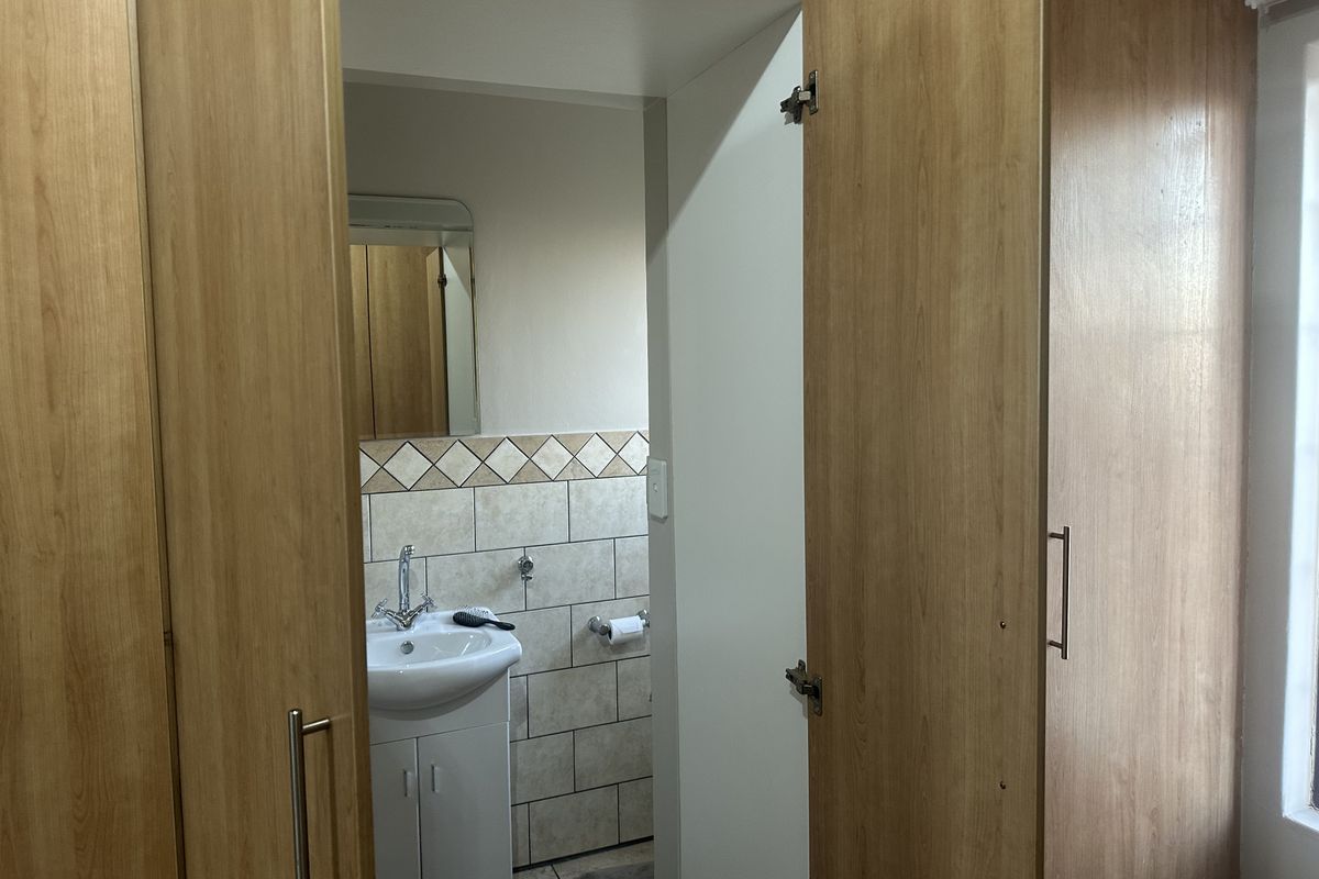 A bathroom featuring a pedestal basin with tiled splashback, complemented by built-in wooden cupboards providing ample storage space.