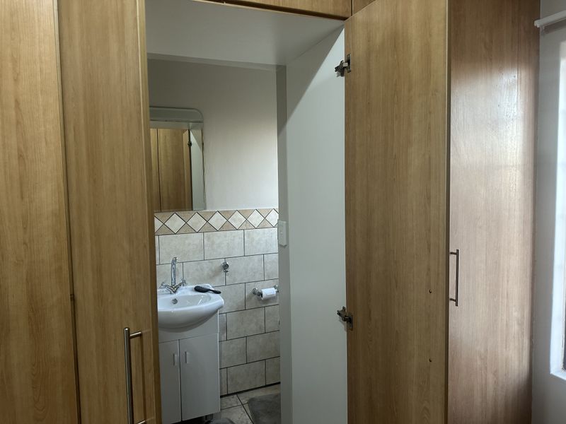 A bathroom featuring a pedestal basin with tiled splashback, complemented by built-in wooden cupboards providing ample storage space.