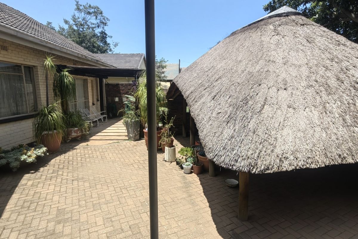Rear exterior view featuring a paved patio area and a traditional thatched lapa structure.