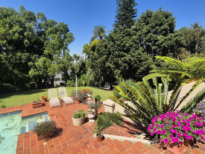 A sunny outdoor pool area featuring a brick-paved patio, established garden landscaping, and a swimming pool, perfect for outdoor relaxation and entertainment.