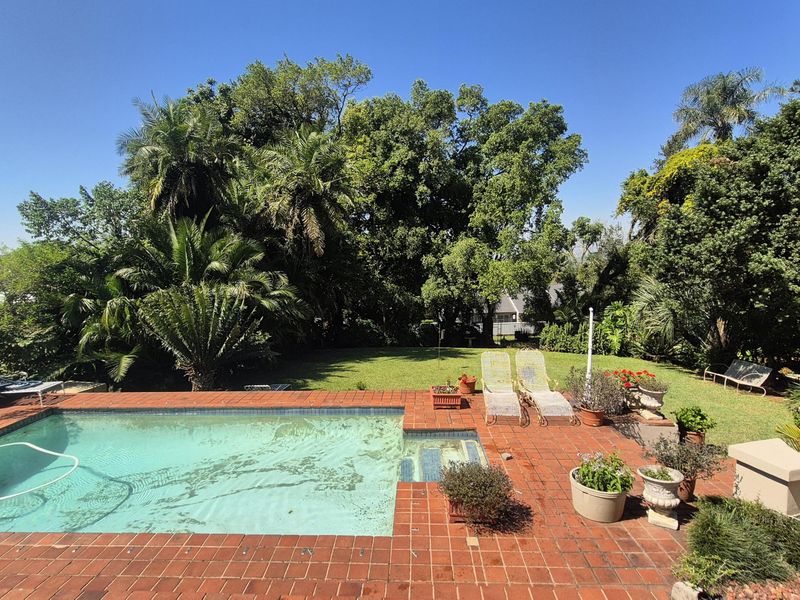 Outdoor pool area featuring a swimming pool with brick coping and a surrounding brick patio set within a mature, landscaped garden.