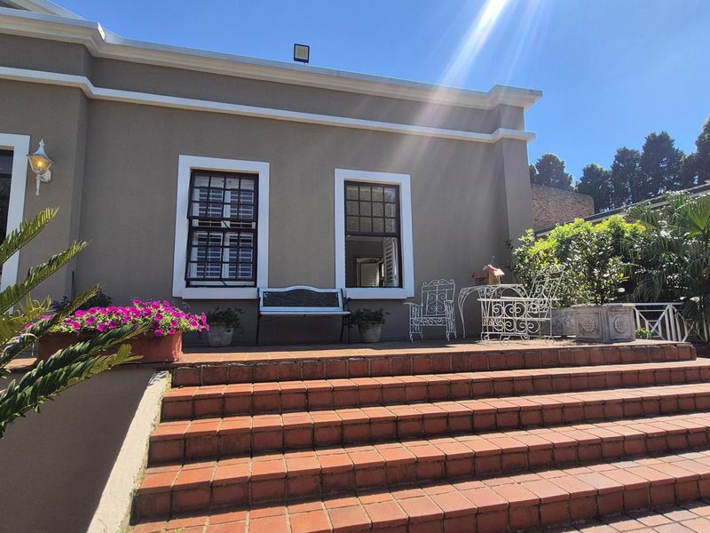 A sunny outdoor patio area featuring terracotta tiled steps leading up to a well-maintained exterior facade with timber-framed windows.