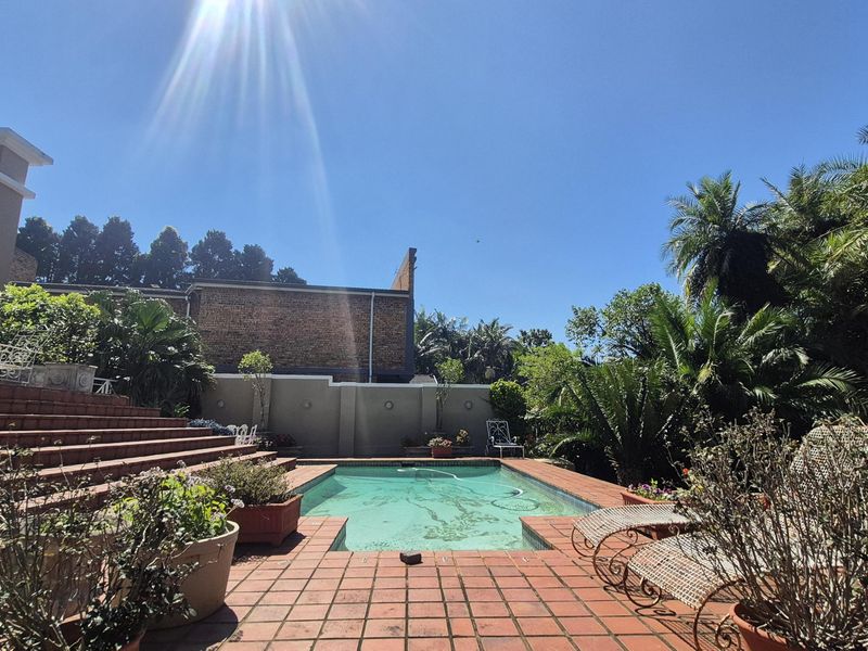 Outdoor pool area featuring a tiled deck, brick retaining steps, and a perimeter wall, set within a landscaped garden environment.