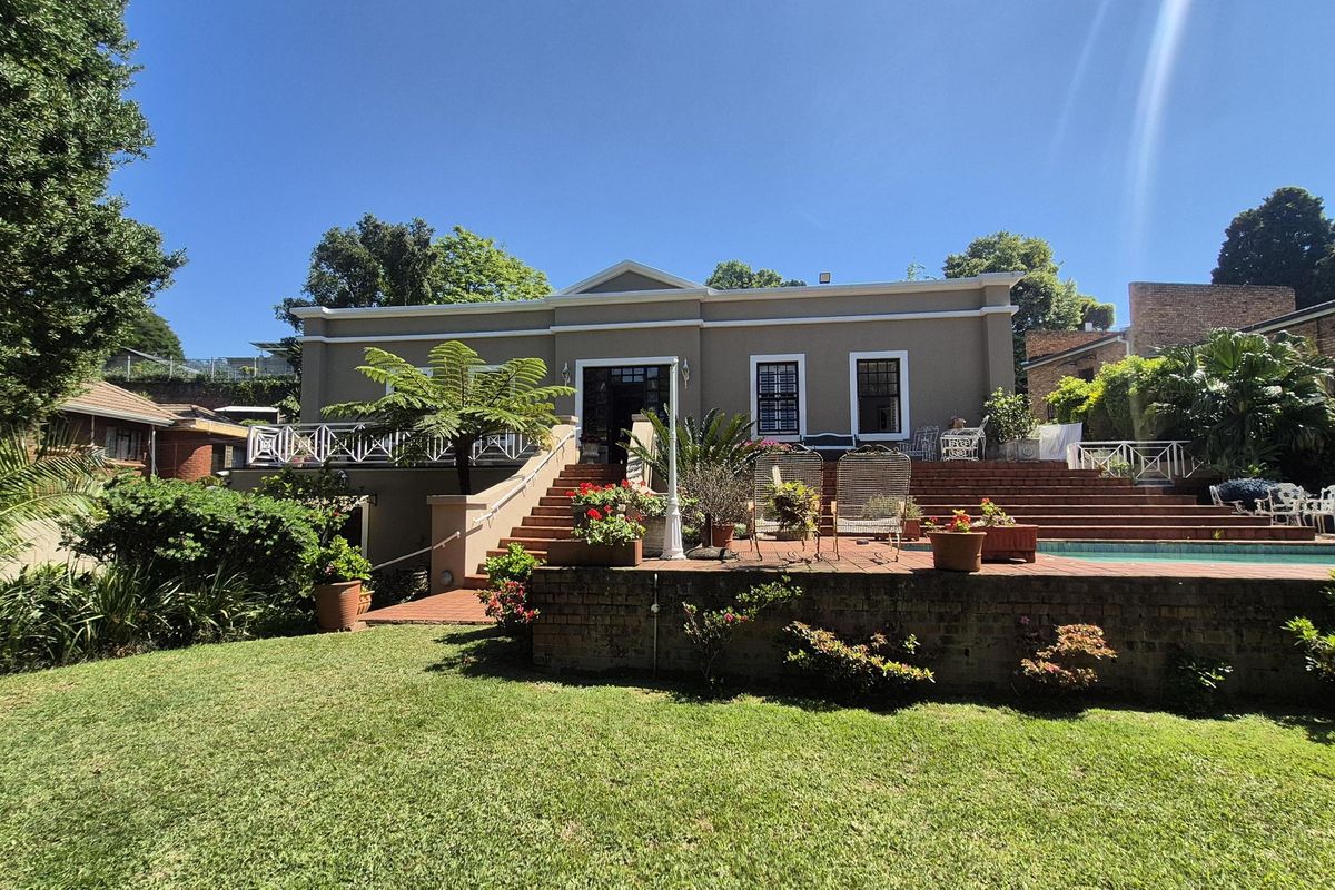 Rear view of the property featuring a raised brick patio, swimming pool, and well-maintained garden area with stairs leading to the main house entrance.