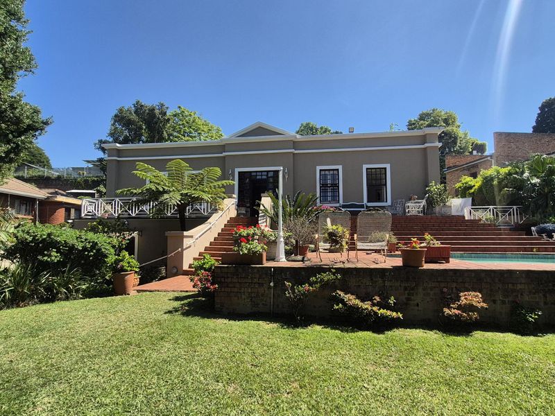 Rear view of the property featuring a raised brick patio, swimming pool, and well-maintained garden area with stairs leading to the main house entrance.