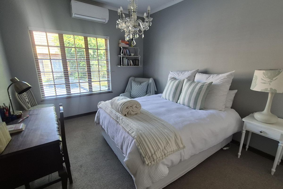 A well-maintained bedroom featuring neutral wall tones, carpeted flooring, a split-system air conditioner, and a decorative chandelier.