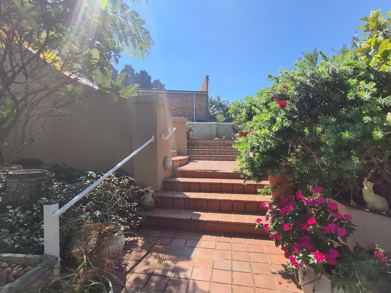 A well-maintained garden area featuring a brick staircase with a metal handrail, leading to an elevated outdoor space surrounded by established landscaping.