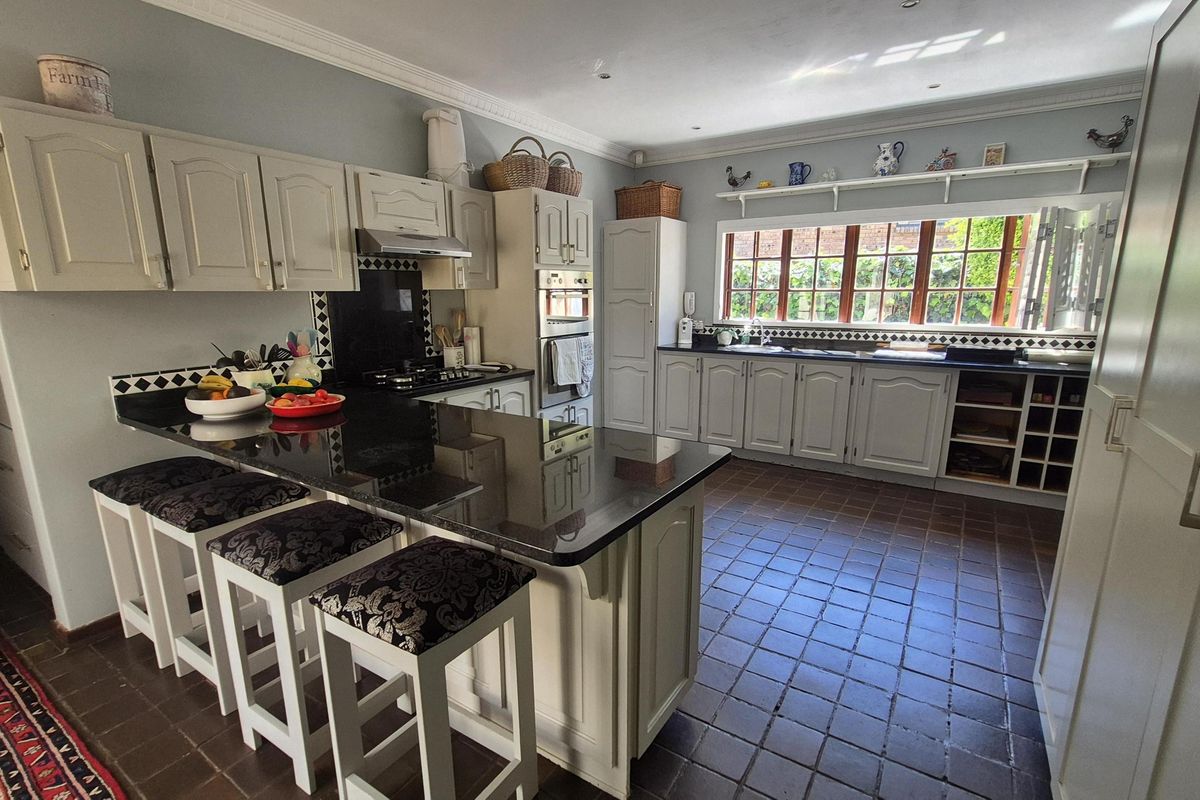Spacious kitchen featuring classic cabinetry, granite countertops, a central island with breakfast bar seating, and large windows overlooking the garden.