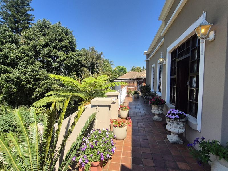 A spacious covered balcony featuring terracotta tiling, wrought iron railings, and wall-mounted lighting, overlooking a lush garden area.