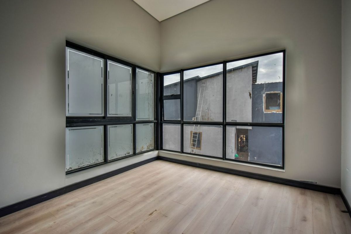 An empty bedroom featuring light wood-look flooring, dark-framed corner windows, and neutral wall finishes.
