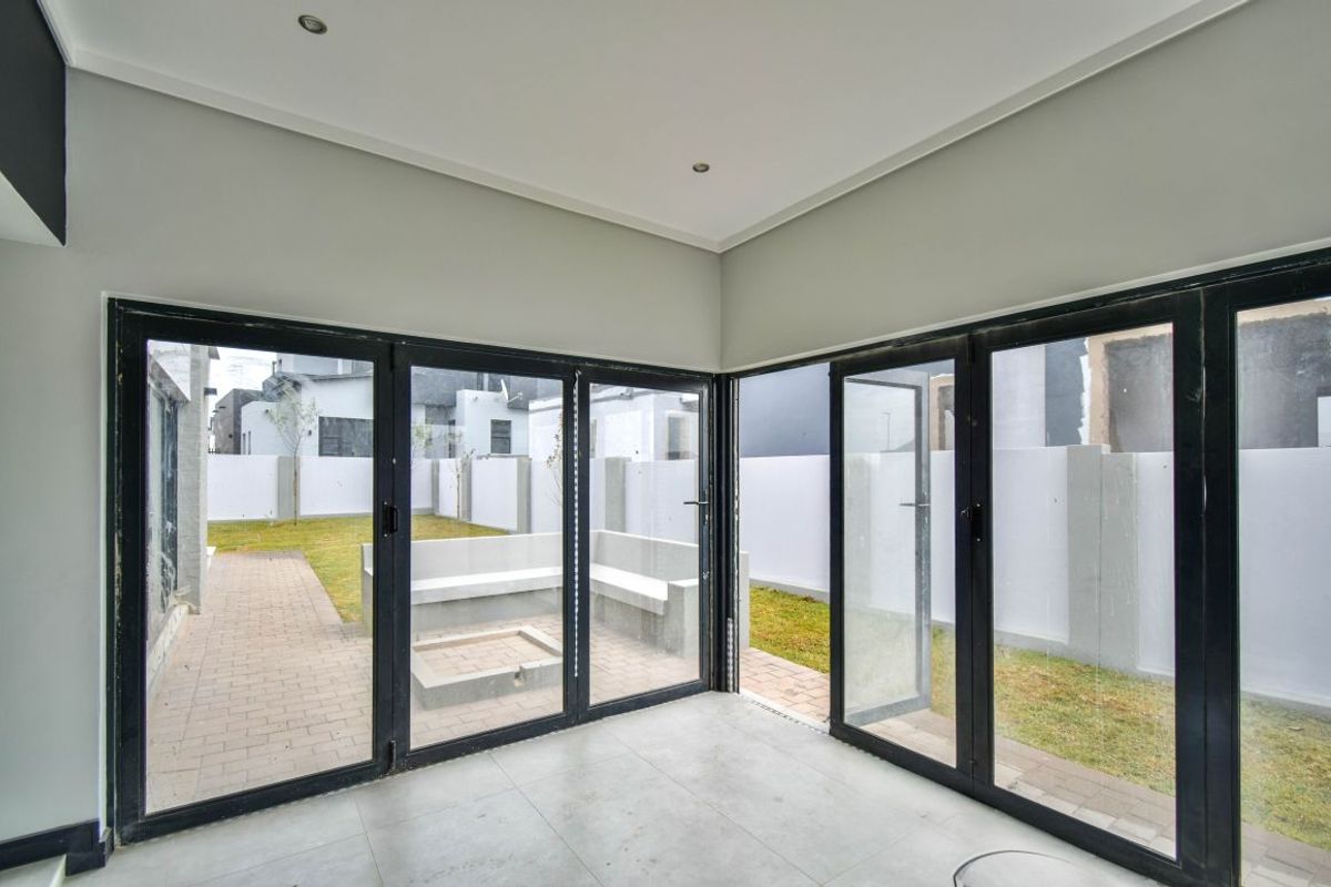 A bright, modern living space featuring large black-framed glass stacker doors that open directly onto a paved patio and garden area.