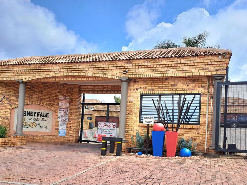 The main entrance gate and security facade of the Honeyvale apartment complex, featuring brick construction, tiled roofing, and secure gated access.
