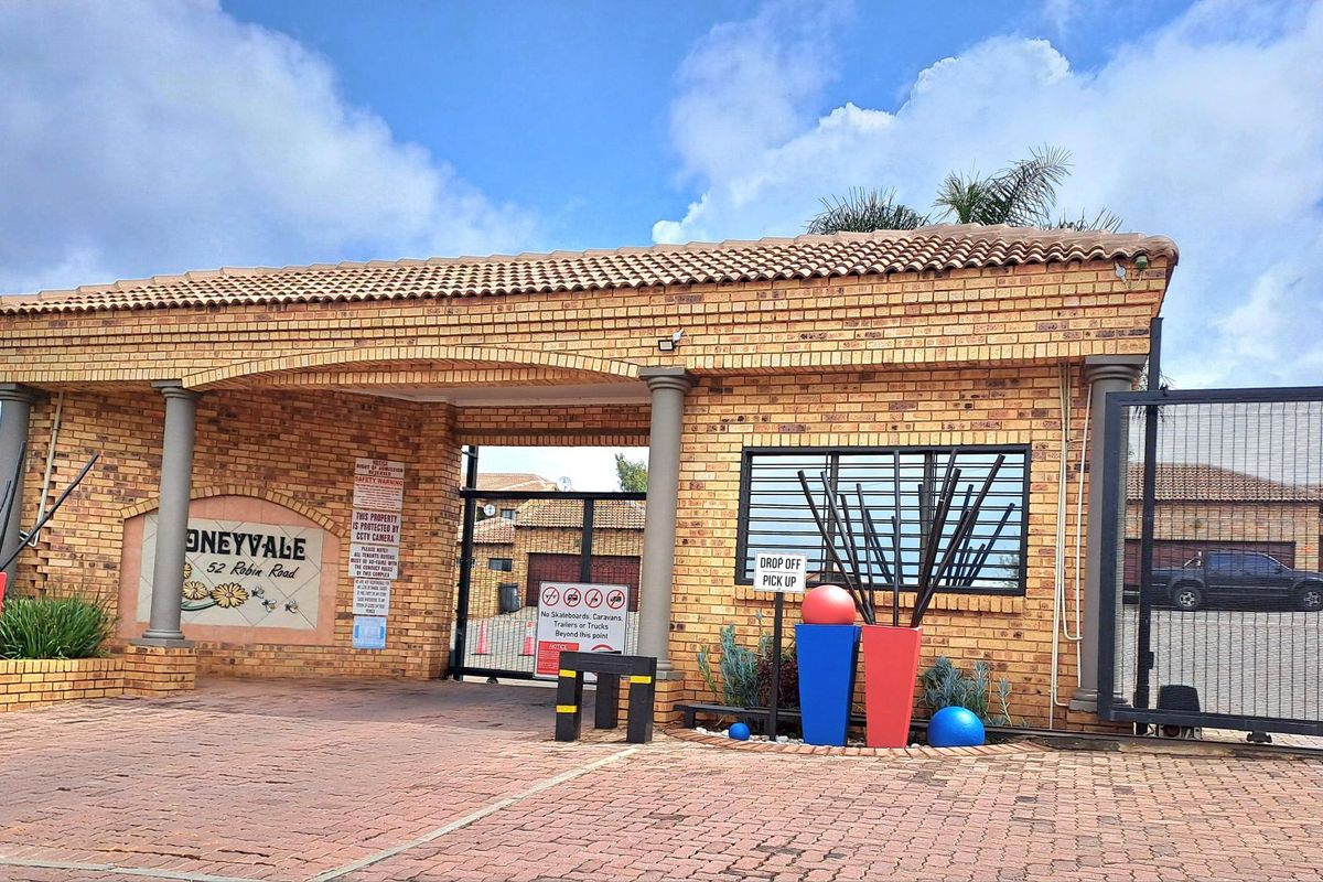 The main entrance gate and security facade of the Honeyvale apartment complex, featuring brick construction, tiled roofing, and secure gated access.