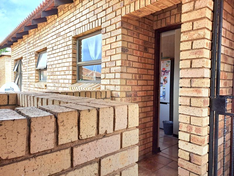 Exterior view of an apartment entrance featuring face brick facade, tiled flooring, and a secure metal gate.