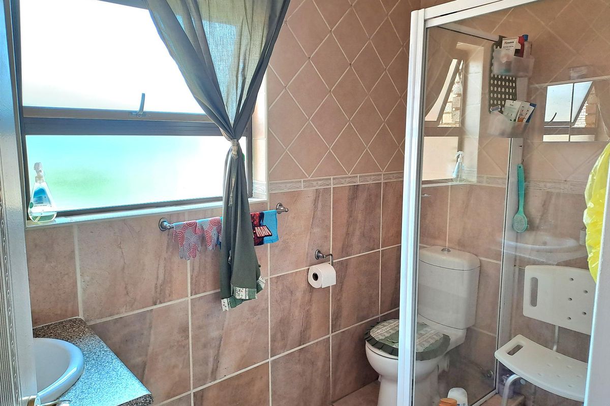 A functional bathroom featuring a glass-enclosed shower, a toilet, and a vanity with a basin, finished with neutral-toned wall and floor tiles.