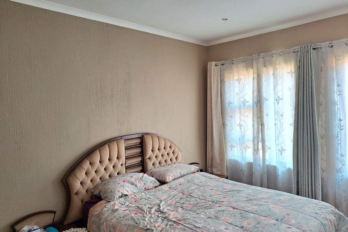 A bedroom featuring textured walls, coved ceiling cornices, and large windows with fitted curtain tracks.