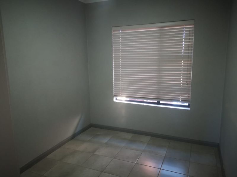 A neutral, empty bedroom featuring tiled flooring and a window fitted with horizontal blinds, offering a clean and versatile space.