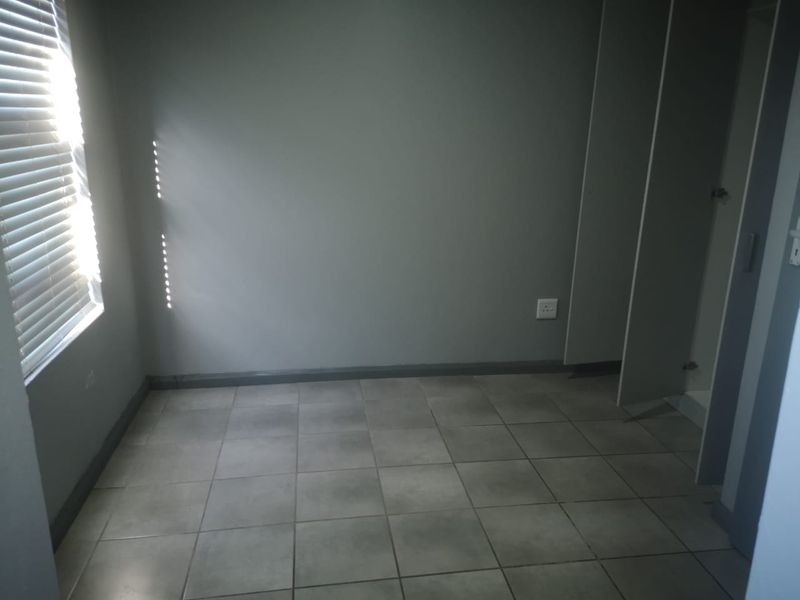 A neutral-toned bedroom featuring tiled flooring, built-in cupboards, and a window fitted with horizontal blinds.