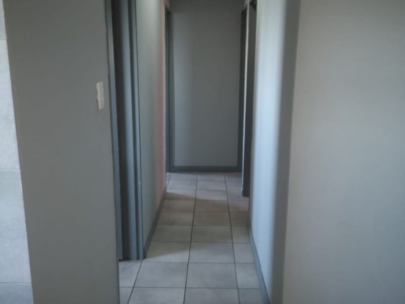 A clean, neutral-toned hallway featuring tiled flooring and recessed ceiling lighting, providing access to multiple rooms within the apartment.