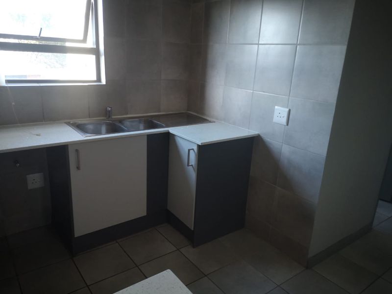 A compact kitchen area featuring built-in cabinetry, a double stainless steel sink, and tiled wall splashbacks with a window for natural light.