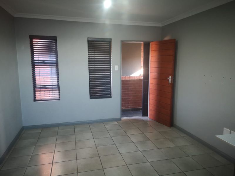 An empty bedroom featuring tiled flooring, two windows with fitted blinds, and a wooden door leading to an outdoor balcony area.