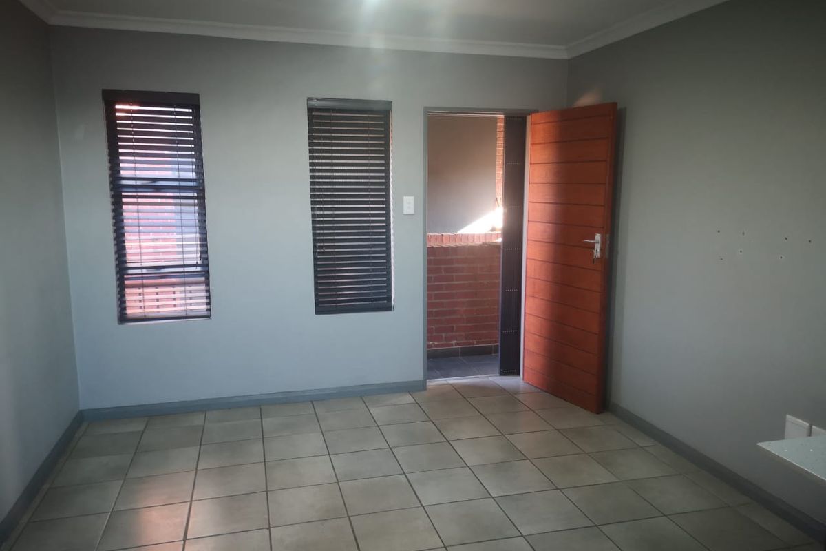An empty bedroom featuring tiled flooring, two windows with fitted blinds, and a wooden door leading to an outdoor balcony area.