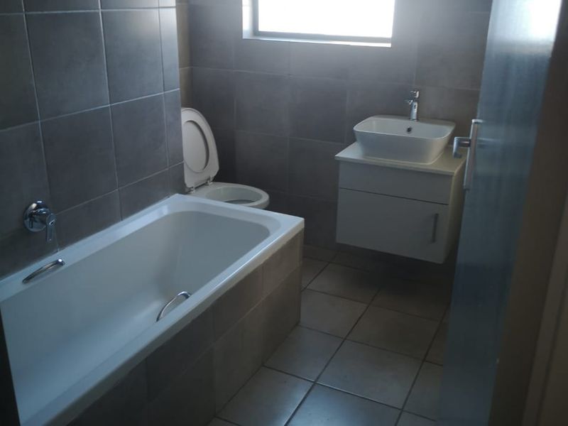 A modern bathroom featuring floor-to-ceiling tiling, a built-in bathtub, a wall-mounted vanity with a basin, and a toilet.