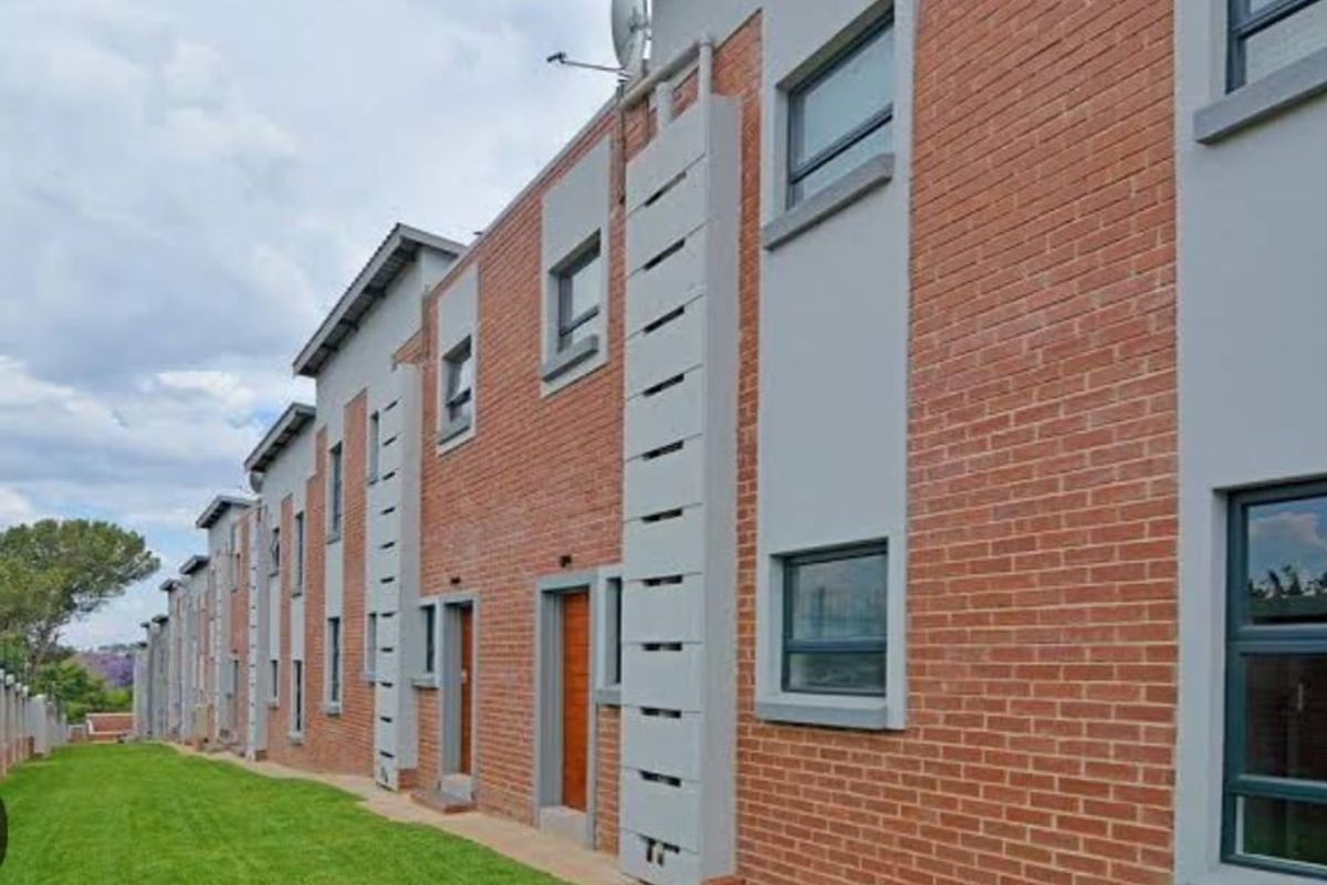 Exterior view of a modern multi-story apartment complex featuring red brick facade, grey plaster accents, and aluminum window frames.
