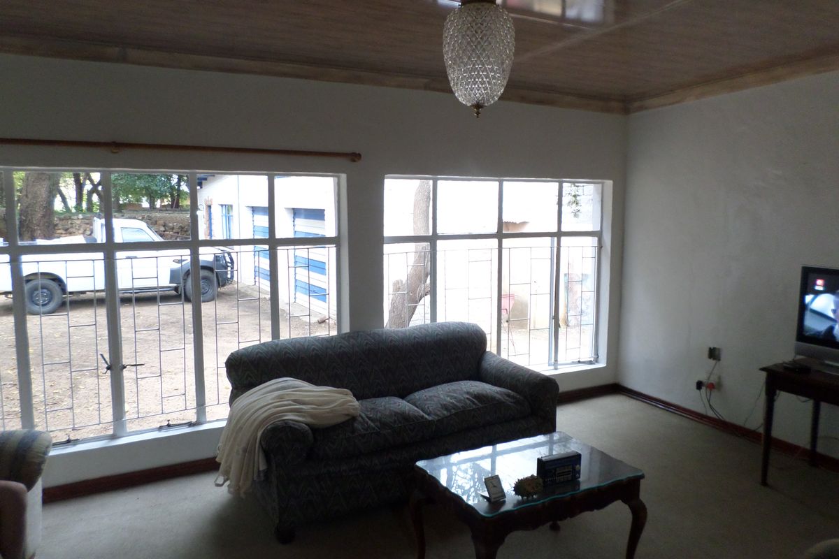 A living room featuring large windows with security bars, a glossy ceiling finish, and a central pendant light fixture.