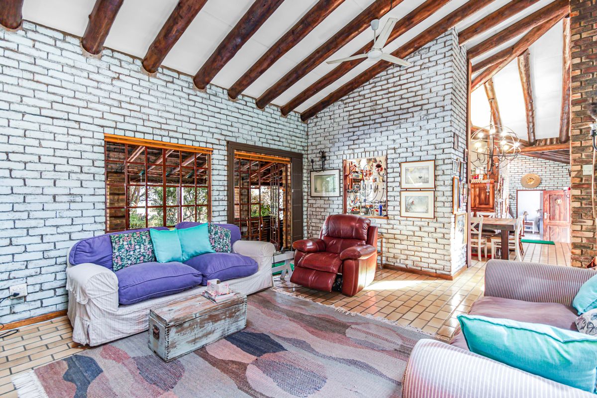 Spacious living area featuring exposed timber ceiling beams, white-painted brick walls, and terracotta floor tiles, creating a rustic and character-filled atmosphere.