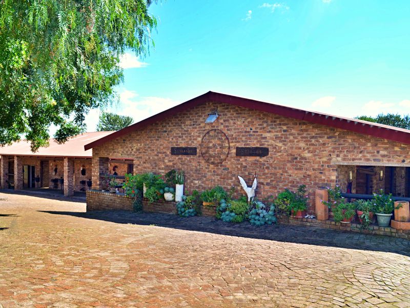 A well-maintained brick stable block featuring a paved courtyard, covered walkways, and established garden beds, characteristic of a rural small holding property.