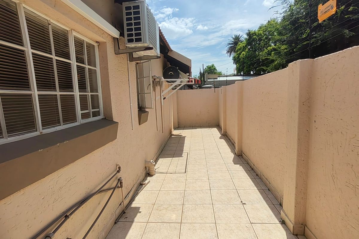 A paved rear courtyard area featuring a boundary wall, external air conditioning unit, and wall-mounted utility fixtures.