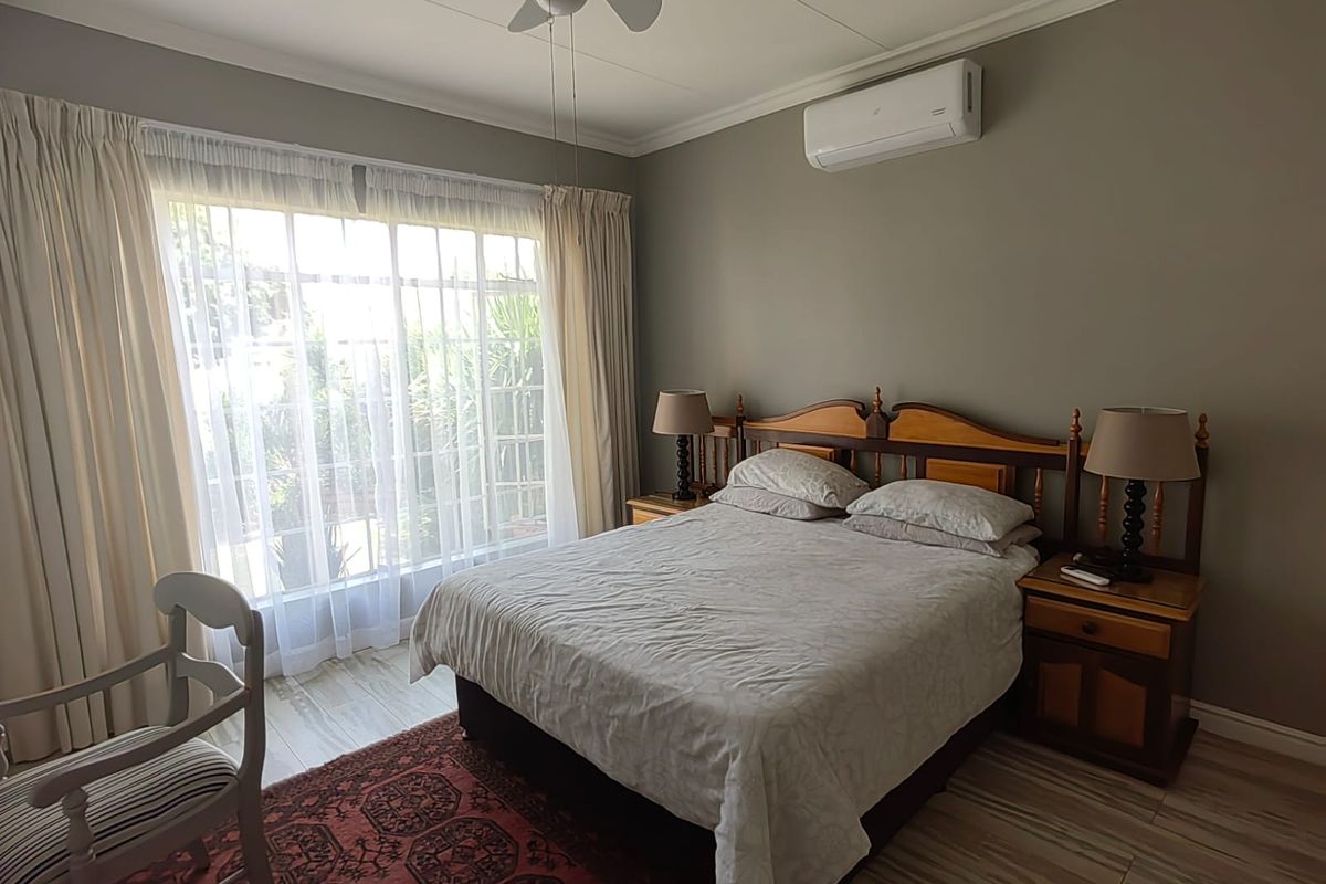 A well-maintained bedroom featuring tiled flooring, a ceiling fan, and a wall-mounted split-system air conditioner, with large windows providing natural light.