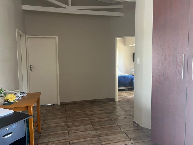 A spacious hallway featuring tiled flooring, exposed ceiling beams, and a built-in cupboard, providing access to adjacent rooms.