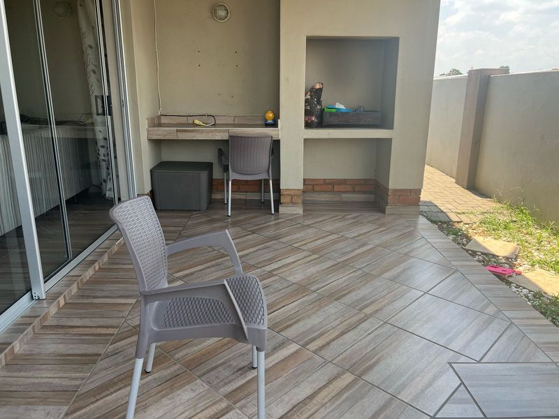 Covered patio area featuring tiled flooring, a built-in braai, and direct access to the interior via sliding glass doors.