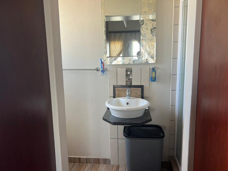 A compact bathroom featuring a modern vessel sink with a granite vanity top, tiled backsplash, and a shower enclosure.