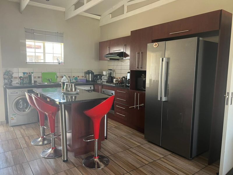 A functional kitchen featuring dark wood cabinetry, granite countertops, tiled flooring, and exposed ceiling beams, providing a practical workspace with integrated appliances.