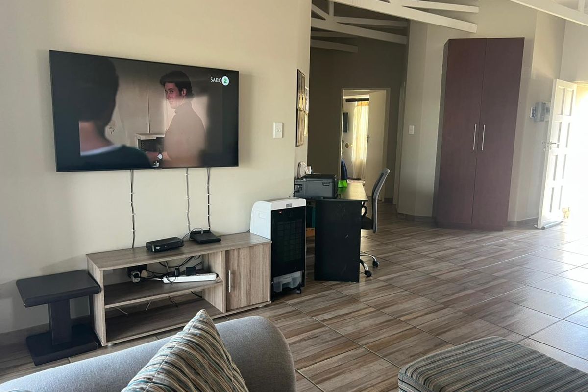 A living area featuring tiled flooring and exposed roof trusses, with a built-in cupboard and neutral wall finishes.